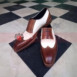 May include: A pair of brown and white leather Oxford shoes with wingtip detailing. The shoes have a lace-up closure and a brogue pattern.