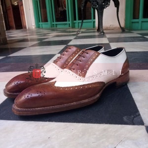 May include: Brown and white leather brogue shoes with a wingtip design. The shoes have a lace-up closure and a brown sole.