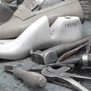 May include: A white shoe last with the number 39556 printed on it. The last is sitting on a table with various tools, including a hammer, pliers, and a screwdriver.