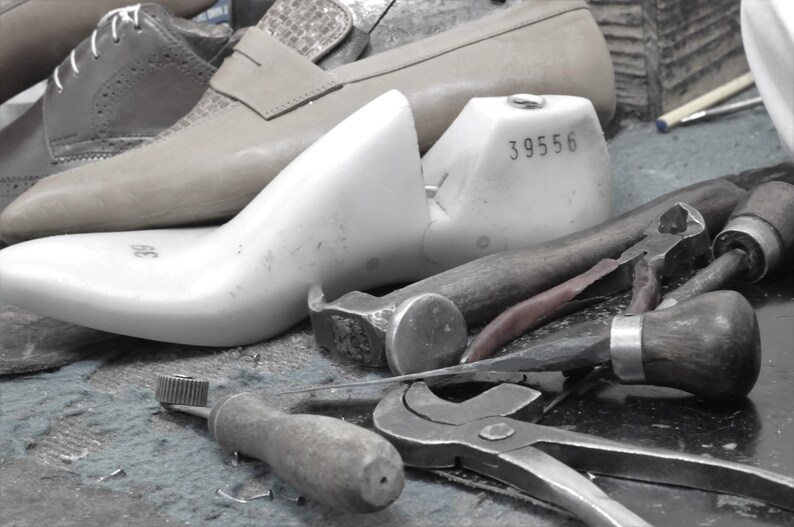 May include: A white shoe last with the number 39556 printed on it. The last is sitting on a table with various tools, including a hammer, pliers, and a screwdriver.
