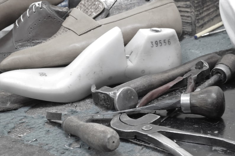 May include: A white shoe last with the number 39556 on it. The last is surrounded by various tools used for shoemaking, including a hammer, pliers, and a screwdriver.