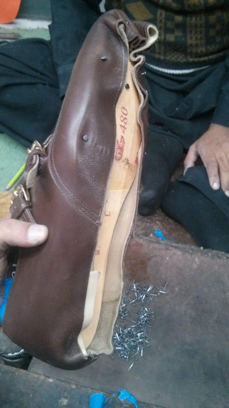 May include: A brown leather boot with a wooden last inside. The boot is open and the last is visible. The last is labeled "G 480". There are many small metal tacks scattered on the floor.