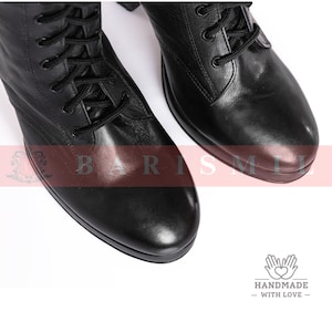 May include: Close-up of two black leather combat boots with black laces. The boots have a rounded toe and a sturdy sole. The image is on a white background. The boots are handmade with love.