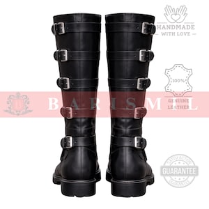 May include: A pair of black leather knee-high boots with multiple buckle straps. The boots have a round toe and a sturdy sole. The image includes the text "HANDMADE WITH LOVE" and "GENUINE LEATHER".