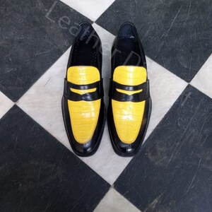 May include: A pair of black leather loafers with yellow crocodile-embossed leather toes. The shoes are on a black and white chequered floor.