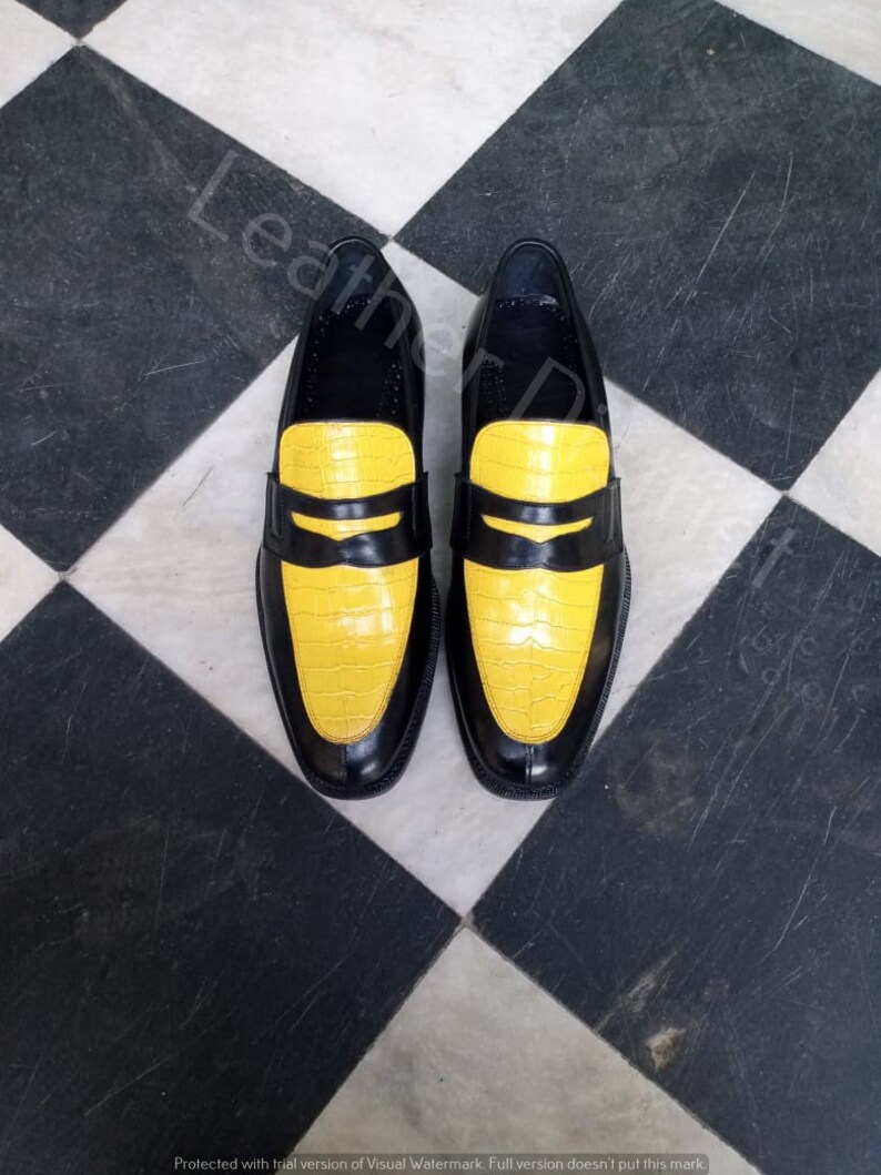 May include: A pair of black leather loafers with yellow crocodile-embossed leather toes. The shoes are on a black and white chequered floor.