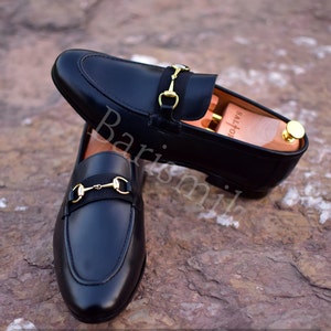 Op de afbeelding: Zwarte leren loafers met een gouden paardenbit detail. De loafers hebben een spitse neus en een slip-on ontwerp.