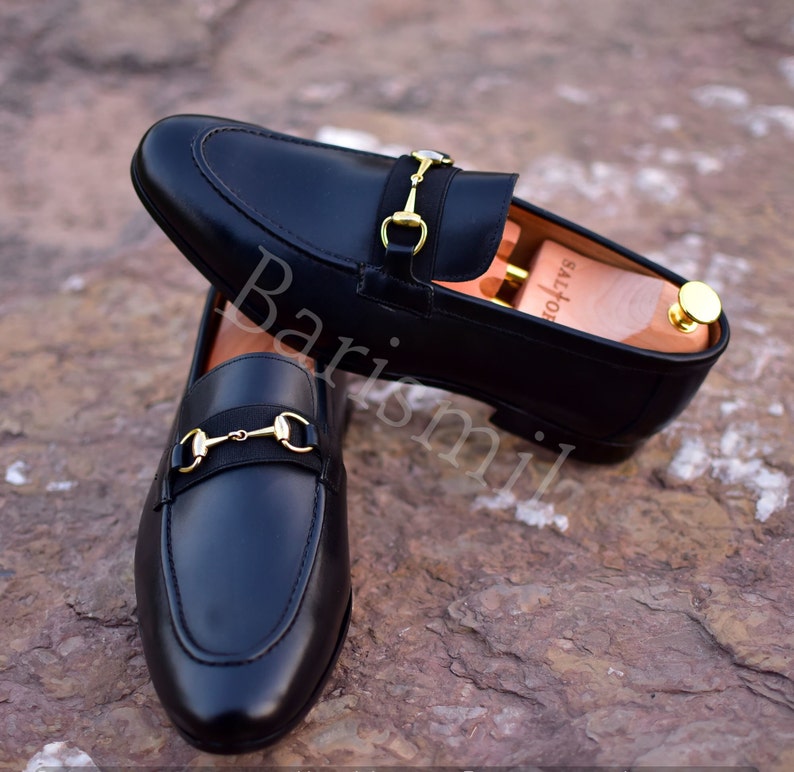 Op de afbeelding: Zwarte leren loafers met een gouden paardenbit detail. De loafers hebben een spitse neus en een slip-on ontwerp.