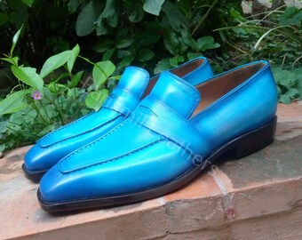 May include: A pair of blue leather loafers with a square toe and a black sole. The loafers have a single strap across the top and a stitched detail around the toe.