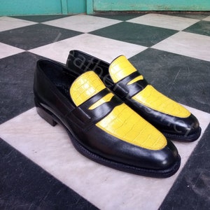 May include: A pair of black leather loafers with yellow leather accents. The loafers have a pointed toe and a black rubber sole.