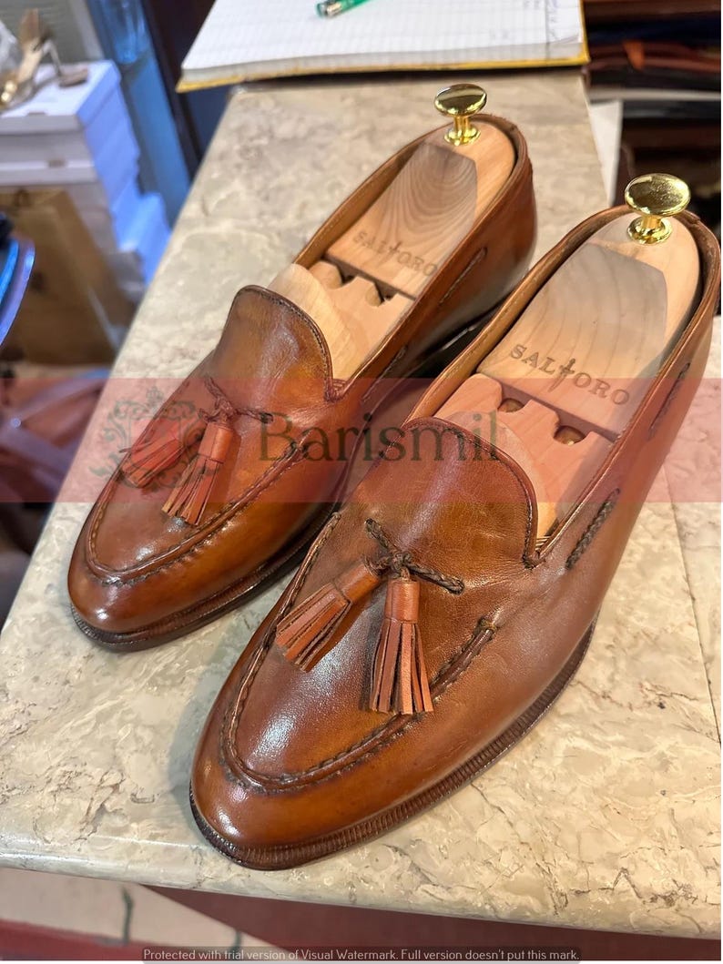 May include: A pair of brown leather tassel loafers with wooden shoe trees inside. The shoe trees are labeled "Saltoro".