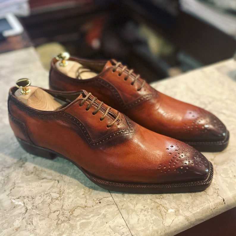May include: A pair of brown leather lace-up shoes with a wingtip design. The shoes have a brogue pattern and a pointed toe.