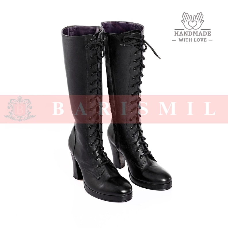 May include: A pair of black leather knee-high boots with a lace-up design. The boots have a high heel and a platform sole. The boots are displayed on a white background. The boots are labeled "HANDMADE - WITH LOVE -."