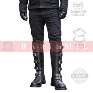 May include: Black leather knee-high boots with multiple silver buckles. The boots have a sturdy sole and are worn with black jeans. The image also includes the text "HANDMADE WITH LOVE" and "GENUINE LEATHER".