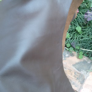 May include: A piece of brown leather with a smooth, textured surface. The leather is folded in half and held by a hand.