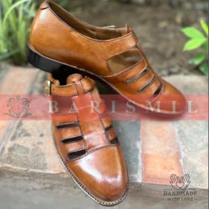 Puede incluir: Sandalias de cuero marr&oacute;n con un dise&ntilde;o recortado. Las sandalias tienen un cierre de hebilla y una suela negra. La imagen incluye el texto "BARIS MIL" y "HANDMADE - WITH LOVE".