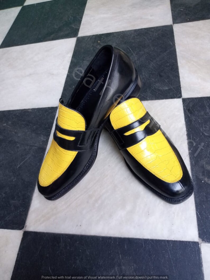 May include: A pair of black leather loafers with yellow crocodile-embossed leather accents. The loafers have a classic penny loafer design with a strap across the top.