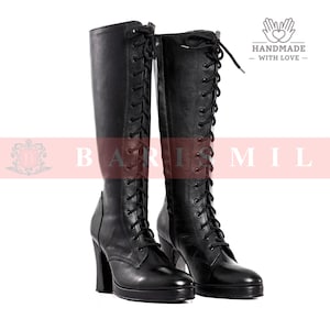 May include: A pair of black leather knee-high boots with lace-up detailing. The boots have a high heel and a rounded toe. The image also includes the text "BARI MIL" and "HANDMADE - WITH LOVE -."