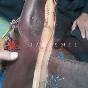 May include: A brown leather shoe with a wooden last inside. The shoe is being worked on by a cobbler. There are nails scattered on the floor.
