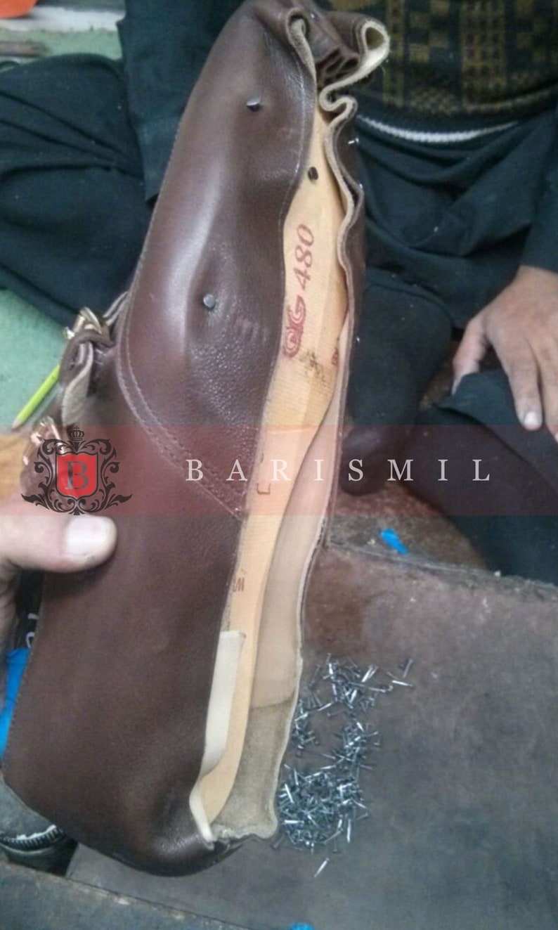 May include: A brown leather shoe with a wooden last inside. The shoe is being worked on by a cobbler. There are nails scattered on the floor.
