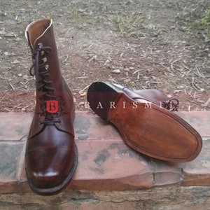 May include: Brown leather lace-up boots with a pointed toe and a thick sole. The boots are made of high-quality leather and have a classic design. The boots are shown on a brick surface.