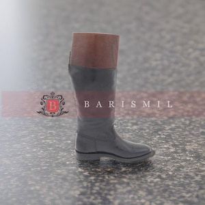 Puede incluir: Un par de botas de montar de cuero negro con parte superior de cuero marrón. Las botas tienen un tacón bajo y una punta puntiaguda.