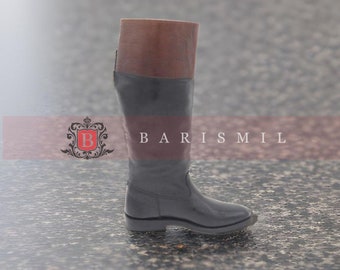 May include: A pair of black leather riding boots with a brown leather top. The boots have a low heel and a pointed toe.