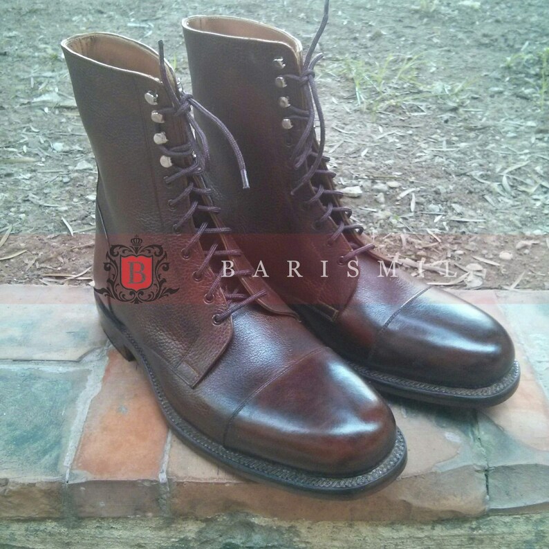 May include: A pair of brown leather lace-up boots with a cap toe. The boots have a textured leather upper and a contrasting brown leather heel.
