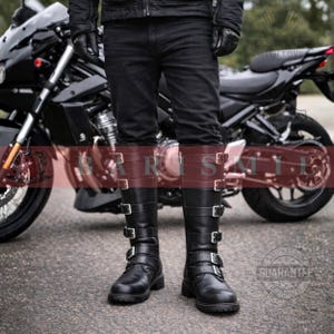 May include: Black leather knee-high boots with multiple silver buckles. The boots have a brown leather band at the top. The boots are worn with black jeans. A black motorcycle is in the background.