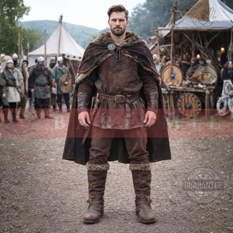May include: A full-length shot of a person in a brown Viking costume. The outfit includes a fur-lined cape, tunic, pants, and boots. A belt with a large buckle and a small knife are visible. The background shows a historical reenactment with tents and other people.