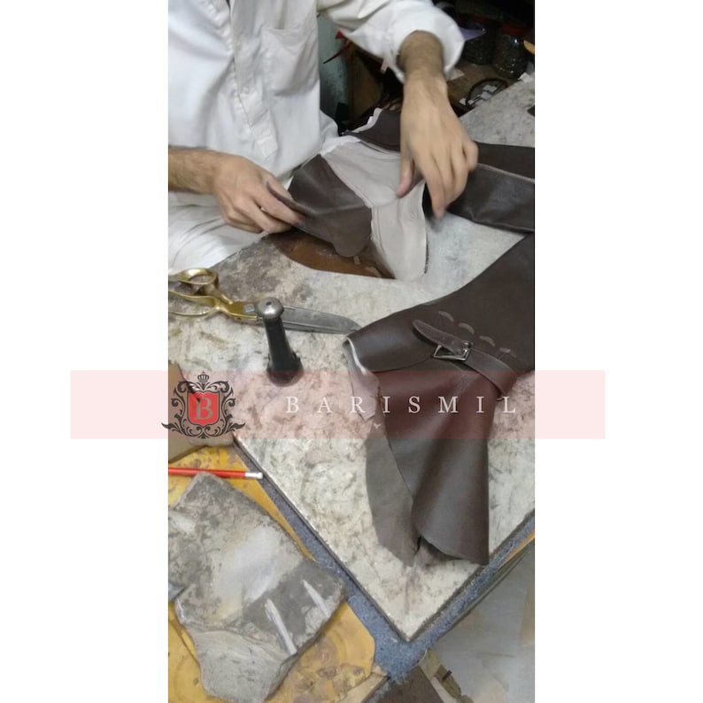 Puede incluir: Un artesano trabajando en una bota de cuero marr&oacute;n, con hebilla y detalle de correa. La imagen muestra la construcci&oacute;n de la bota, con herramientas como tijeras y un mazo visibles. La marca "BARISMIL" tambi&eacute;n es visible.