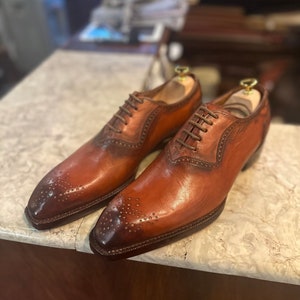May include: A pair of brown leather oxford shoes with brogue detailing and lace-up closures. The shoes have a pointed toe and a polished finish.