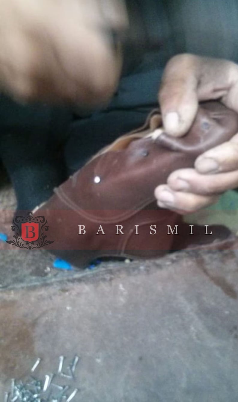 May include: A close-up of a brown leather boot being worked on by a shoemaker. The boot has a white stitch detail and the text "BARIS MIL" is visible on the side.