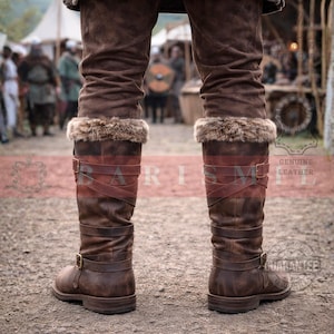 May include: Brown leather knee-high boots with fur trim. The boots feature buckle closures and crisscross straps. The image shows the back view of the boots, with a blurred background of people and buildings.