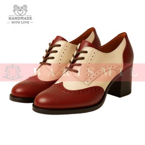 K&ouml;nnte beinhalten: Zweifarbige Oxford-Schuhe aus Leder mit Blockabsatz. Die Schuhe haben eine bordeauxfarbene Spitze und Ferse, eine cremefarbene Mitte und rosa Akzente. Braune Schn&uuml;rsenkel. Der Text "HANDMADE - WITH LOVE" ist sichtbar.