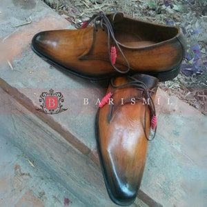 May include: A pair of brown leather lace-up shoes with a pointed toe. The shoes have a distressed look and are decorated with red beads on the laces.