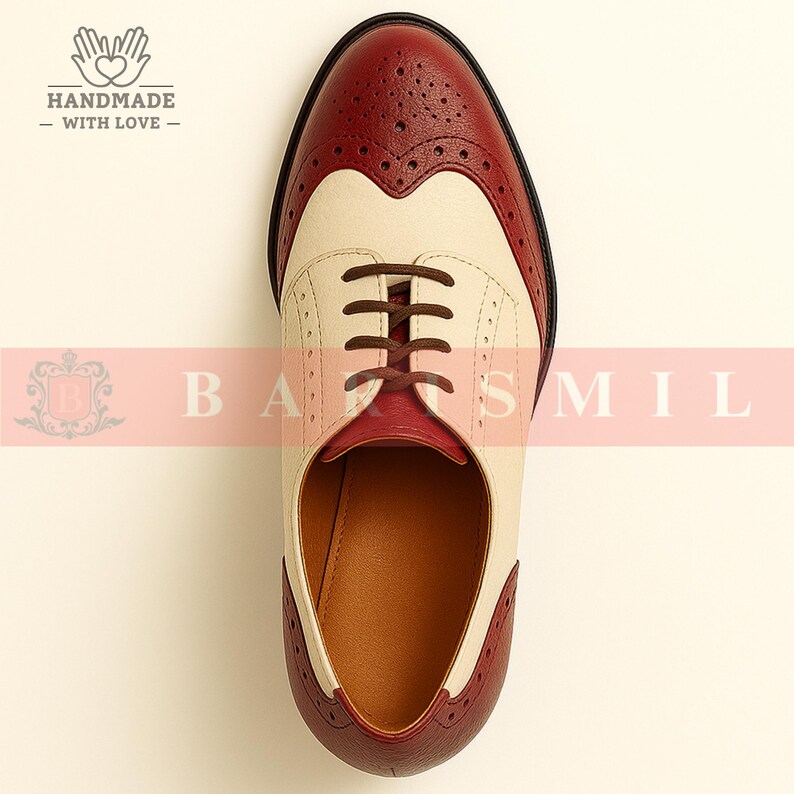 K&ouml;nnte beinhalten: Zweifarbiges Oxford-Schuh aus Leder in Creme und Burgunderrot. Der Schuh hat ein Fl&uuml;gelspitzendesign mit dekorativen Perforationen und braunen Schn&uuml;rsenkeln. Klassischer, formeller Stil.