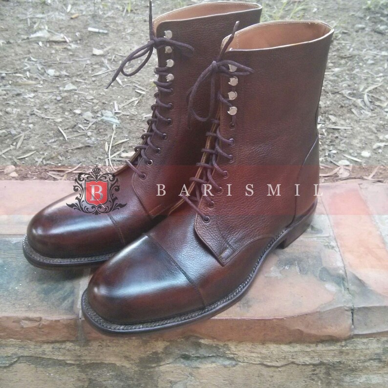 May include: A pair of brown leather lace-up boots with a cap toe design. The boots have a tall shaft and are made of a textured leather.