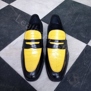 May include: A pair of black leather loafers with yellow crocodile-embossed leather toes. The shoes have a classic loafer design with a penny strap.