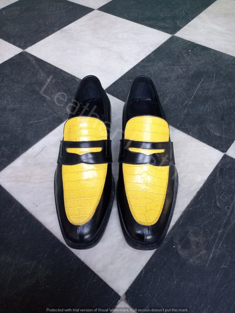 May include: A pair of black leather loafers with yellow crocodile-embossed leather toes. The shoes have a classic loafer design with a penny strap.