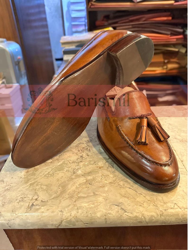 May include: A pair of brown leather tassel loafers with a brown leather sole. The loafers have a tassel detail on the front and a stitched design around the toe.