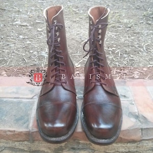 May include: A pair of brown leather lace-up boots with a rounded toe. The boots have a decorative stitching detail around the toe and a lace-up closure with metal eyelets.