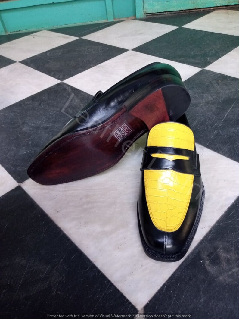 May include: A pair of black leather loafers with a yellow crocodile-embossed leather panel on the toe. The loafers have a brown leather sole and a black leather upper.