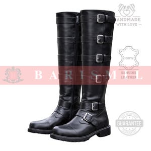 May include: A pair of black leather knee-high boots with multiple straps and silver buckles. The boots have a zipper on the side and a rounded toe. The boots are handmade with genuine leather.