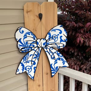 May include: A large blue and white bow with a damask pattern. The bow is made of wood and is hanging on a wooden fence.