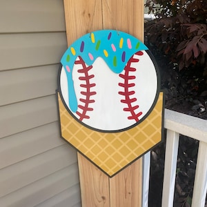 Peut inclure: Panneau de porte en bois sur le thème du baseball. La balle de baseball est blanche avec des coutures rouges, surmontée d'un glaçage bleu et de vermicelles colorés. Le bas est en forme de cornet de gaufre jaune. Une ficelle de jute est attachée pour l'accrocher.