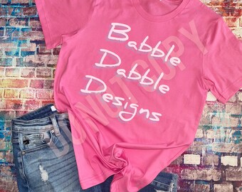 Könnte beinhalten: Pinkes T-Shirt mit dem Text "Babble Drabble Designs" in weiß.