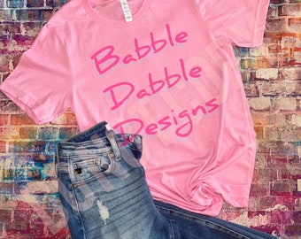 Könnte beinhalten: Pinkes T-Shirt mit dem Text "Babble Dabble Designs" in pinker Schrift.