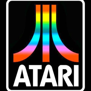 May include: A black and white logo with a rainbow colored graphic of a stylized "A" with the word "ATARI" below it.