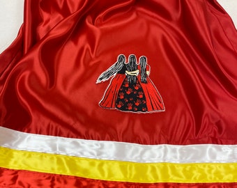 May include: A red satin skirt with a white, yellow, red, and black ribbon trim. The skirt has an embroidered patch of three women with long black hair and red hands.